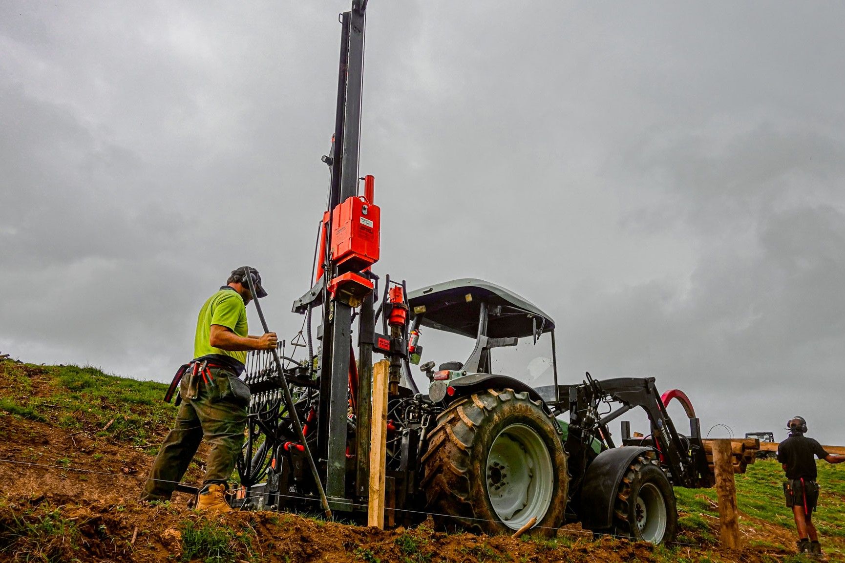 FencePro Ultra G2S hydraulic post driver driving a wooden fence post, showing mast stability and operator control on sloping terrain